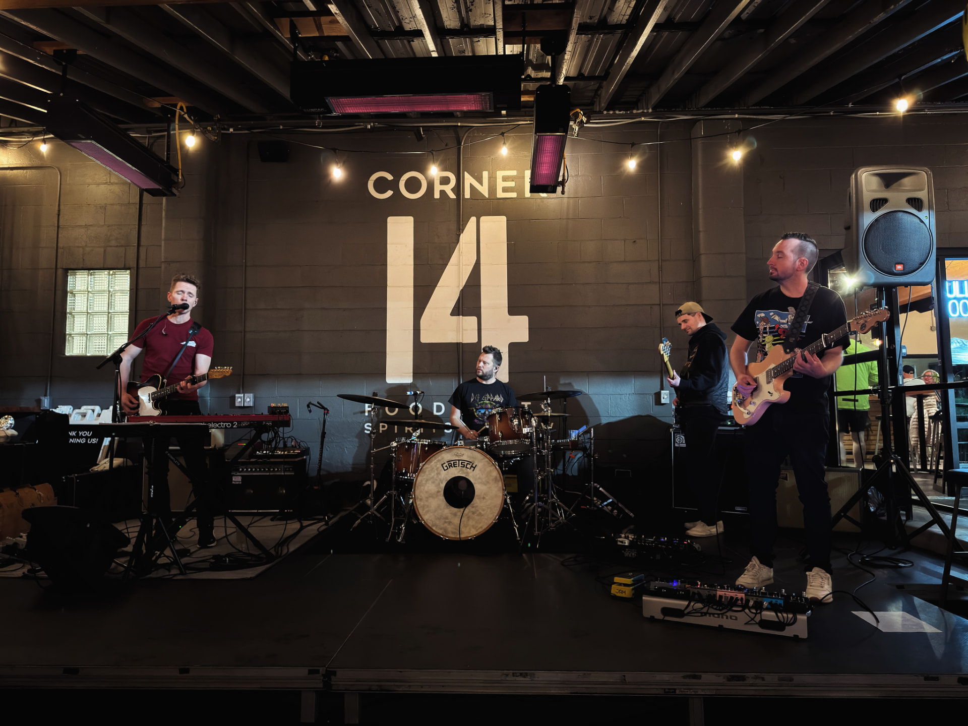 Drift & Flutter performing live on stage at Corner 14 with guitar, drums, and bass in a warm, dimly lit venue